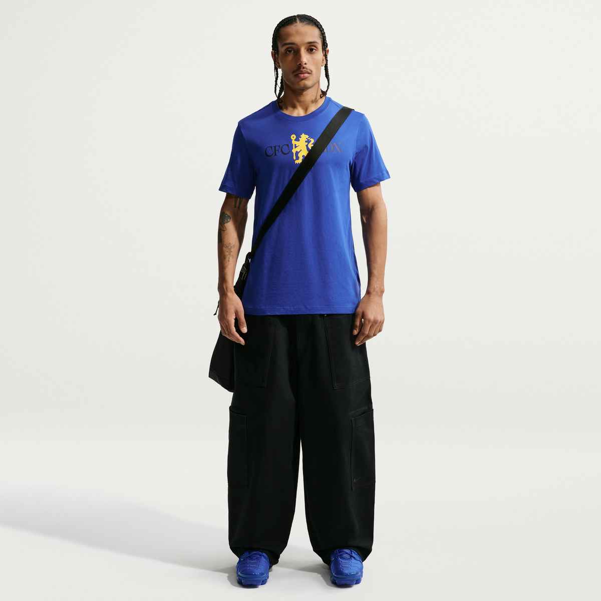Person wearing a blue t-shirt with a logo, black pants, and blue shoes on a white background