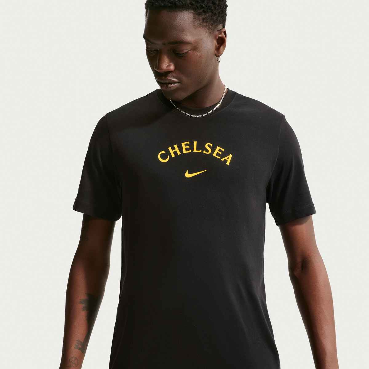 Person wearing a black t-shirt with 'Chelsea' printed on it against a plain background